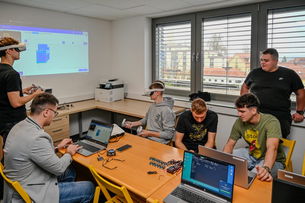 Dogodek projekta UrbanMakerSpace. Ljudje sedijo za mizo in gledajo v računalnik.