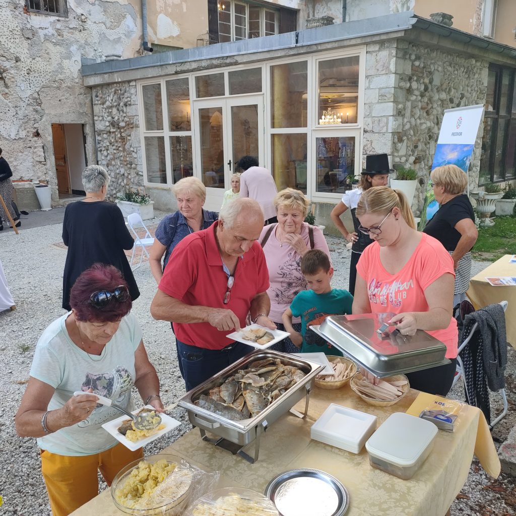 Ljudje okoli mize na prostem posegajo po ribji hrani.
