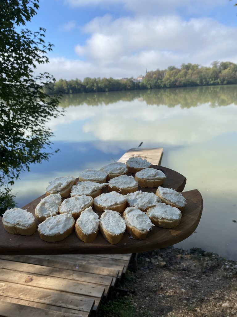 Na leseni deski oblozeni kruhki z ribjim namazom. V ozadju jezero.