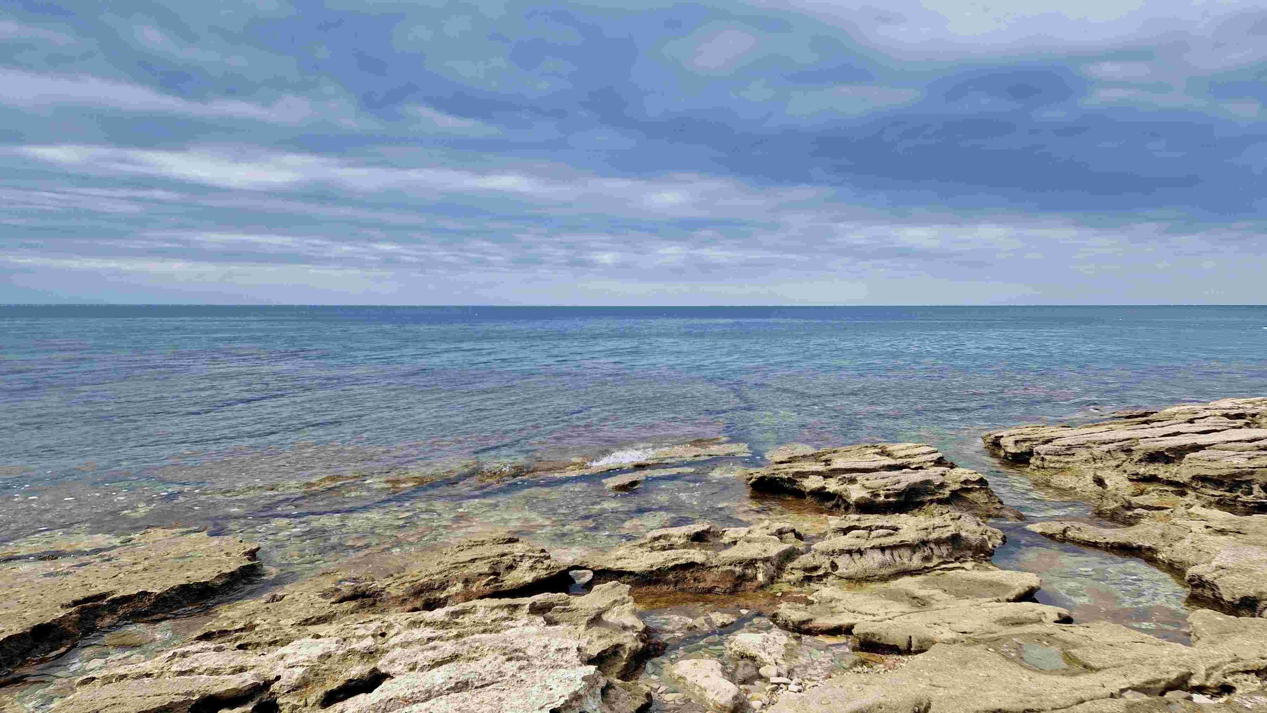 V ospredju kamnita obala v spodnjem delu slike, ki postopoma proti vrhu slike prehaja v morje.