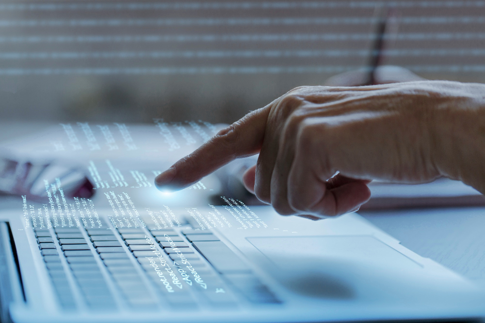 Na mizi prenosni računalnik, bliža se mu ženska roka z iztegnjenim kazalcem.