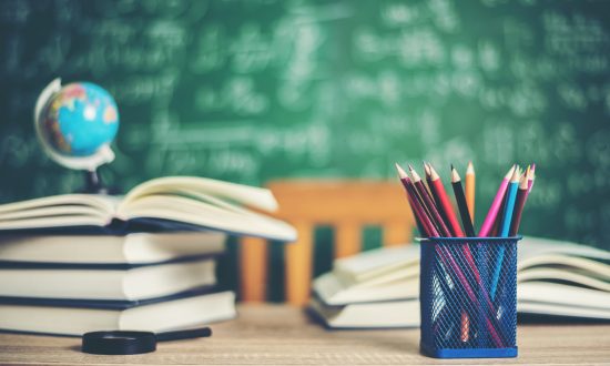 Knjiga, svinčniki in v ozadju šolska tabla.